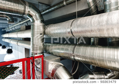 Silver ventilation pipes hanging from the ceiling inside the building 98863479