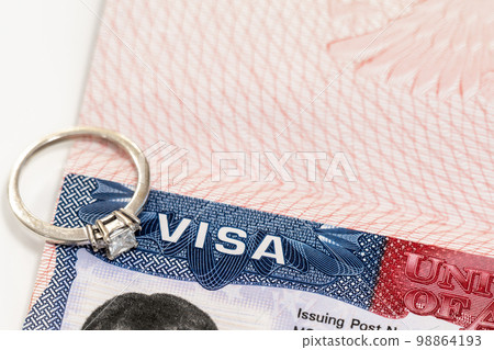 Engagement ring on top of US entry visa sticker in a passport. Conceptual photo for fiance visa and immigration 98864193