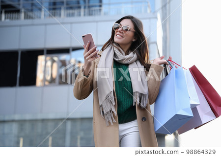 Beautiful young woman with shopping bags and smartphone outdoors Beautiful young woman with shopping bags and smartphone outdoors 98864329