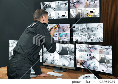 Security guard with portable transmitter monitoring modern CCTV cameras indoors Security guard with portable transmitter monitoring modern CCTV cameras indoors 98865985