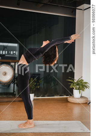 A girl in a black sports uniform does yoga standing on a mat in the gym A girl in a black sports uniform does yoga standing on a mat in the gym 98866077