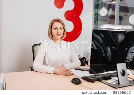 A blonde woman works on a computer behind a worker in an open office. A blonde woman works on a computer behind a worker in an open office. 98866697