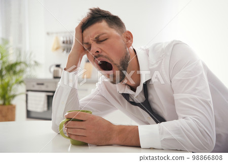 Sleepy man with cup of drink at home in morning 98866808