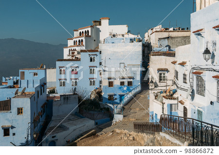 Outskirts of the old city are multi-storey buildings with white and blue walls of various shades. Broken road in potholes. Empty ancient city in the morning is flooded with sunlight. Outskirts of the old city are multi-storey buildings with white and blue walls of various shades. Broken road in potholes. Empty ancient city in the morning is flooded with sunlight. 98866872