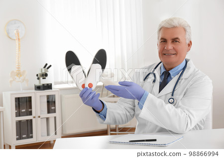 Senior male orthopedist showing insoles in clinic 98866994