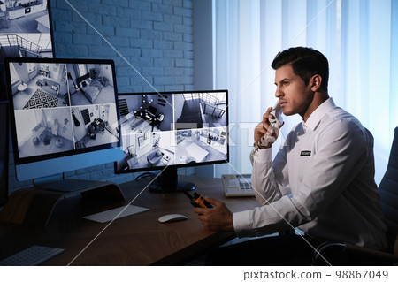 Male security guard talking by telephone near monitors at workplace Male security guard talking by telephone near monitors at workplace 98867049