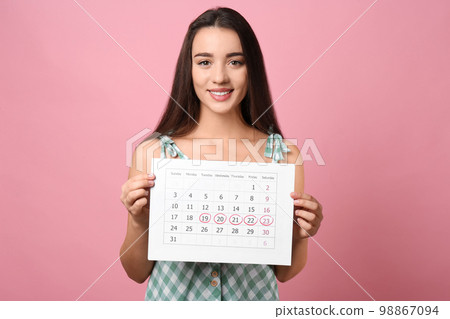 Young woman holding calendar with marked menstrual cycle days on pink background 98867094