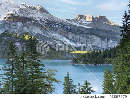 Idyllic morning view of the lake Oeschinensee. Location Swiss alps, Switzerland, Kandersteg district. Blue mountain lake with pine trees and mountains in background. 98867379