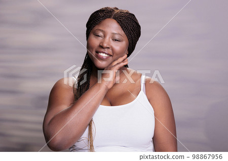 Curvy woman touching smooth hydrated skin after skincare procedures and looking at camera. Plus size african american model holding palm on face after cosmetology treatment Curvy woman touching smooth hydrated skin after skincare procedures and looking at camera. Plus size african american model holding palm on face after cosmetology treatment 98867956