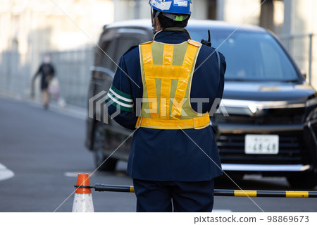 A traffic director wearing a yellow reflective vest guiding traffic at a construction site 98869673