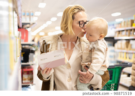 Caucasian mother shopping with her infant baby boy child choosing products in department of supermarket grocery store 98871519