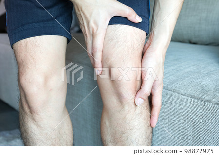 Knee pain. A man standing at home. Hands-on knees. he massages his knees to relieve pain. Knee pain. A man standing at home. Hands-on knees. he massages his knees to relieve pain. 98872975