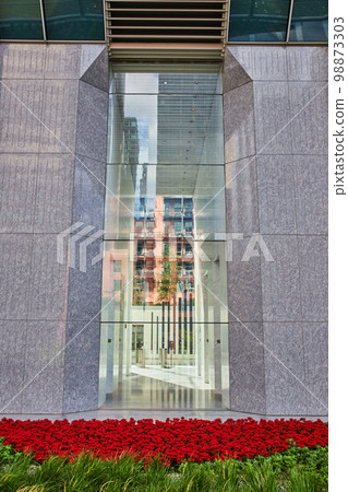 View outside large building with glass view into fancy lobby and red flowers outside 98873303