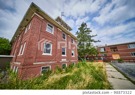 Three story abandoned brick buildings with overgrown fields Three story abandoned brick buildings with overgrown fields 98873322