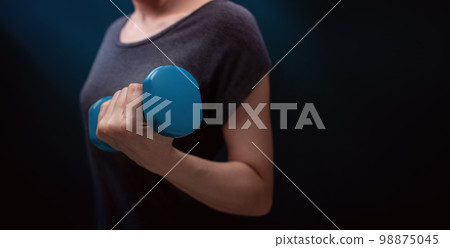 Exercising, Workout with Dumbbell. Sport and Recreation Concept. Close-up of Woman with blue Dumbbell in Dark Room at Home or Gym 98875045