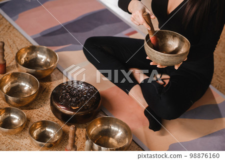 Close-up of a woman's hands sitting in a lotus position using a singing bowl indoors. Relaxation and meditation. Sound therapy, alternative medicine. Tibetan Bowls 98876160
