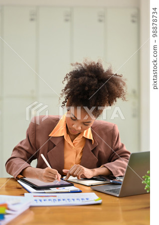 Focused female accountant working with financial document and using digital tablet at office 98878734