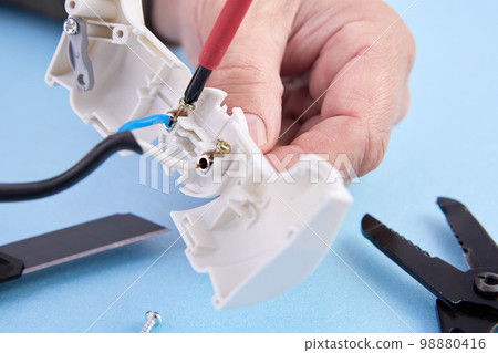 Connecting electrical wire to collapsible electric plug, electrician tightens fixing bolt. Connecting electrical wire to collapsible electric plug, electrician tightens fixing bolt. 98880416