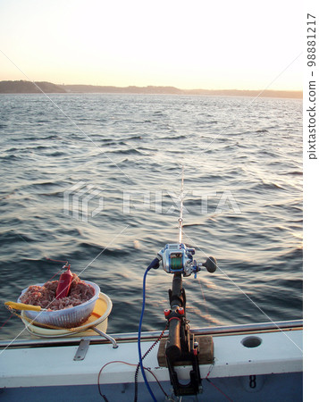 清晨的一艘漁船，一個釣魚座（魚竿、漁線輪、水桶）移動到海中朝陽燦爛的地方。 98881217