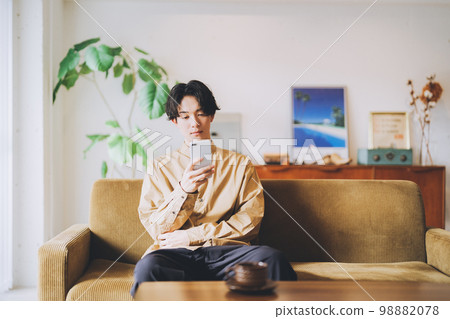 A man sitting on the couch and looking at his smartphone A man sitting on the couch and looking at his smartphone 98882078