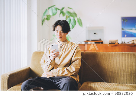 A man sitting on the couch and looking at his smartphone 98882080