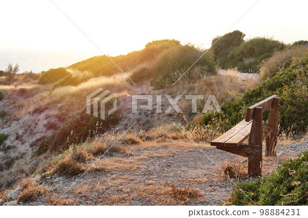 Close-up shot of a wooden bench standing on a mountain at the beach of azure mediterranean sea and surrounded by a beautiful nature of Cyprus. 98884231
