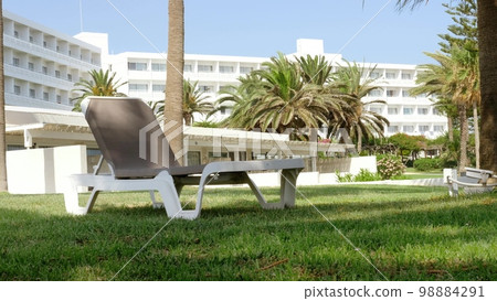 Comfortable deck chair for an ideal rest and sunbathing in a lounge zone of a hotel with green grass and palms. Mediterranean sea, Cyprus. Ayia Napa. 98884291