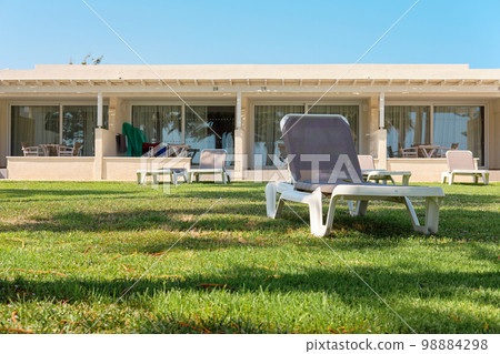 Comfortable deck chair for an ideal rest and sunbathing in a lounge zone of a hotel with green grass and palms. Mediterranean sea, Cyprus. Ayia Napa. 98884298