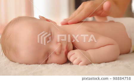 Mother doing massage on her healthy sleeping infant baby. Small caucasian newborn resting and laying on his belly while his mother is performing a massage for his small back and developing muscles. . Mother doing massage on her healthy sleeping infant baby. Small caucasian newborn resting and laying on his belly while his mother is performing a massage for his small back and developing muscles. . 98884758