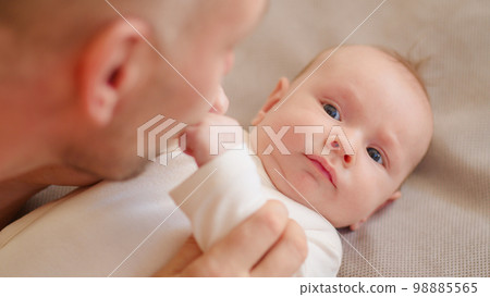 Dad playing with a newborn baby. Cute baby is trying to pronounce sounds while looking at his dad. Face of an active Caucasian baby looking at a parent. Father is playing with his baby. Dad playing with a newborn baby. Cute baby is trying to pronounce sounds while looking at his dad. Face of an active Caucasian baby looking at a parent. Father is playing with his baby. 98885565