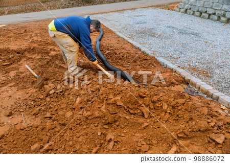When heavy rains are predicted worker digs trench so drainage pipes can be laid during rainy season 98886072