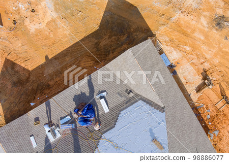 Roofing worker installing new shingles on roof of house during construction 98886077