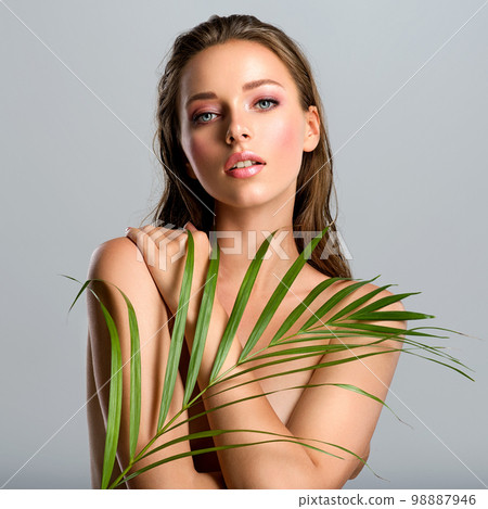 White woman with healthy skin of body and palm leaves. Tanned body of an attractive girl with green plants. Large palm leaves cover the body. 98887946