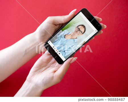 Online expert. Video consultation. Mobile conference. Satisfied smart woman approving with thumb up like gesture on phone screen in hands on red copy space. 98888487
