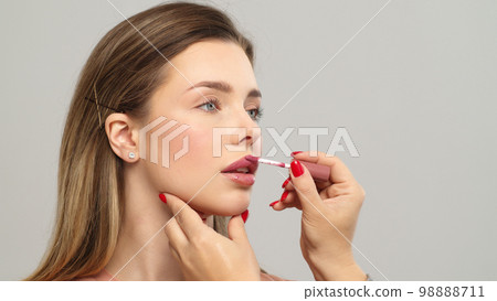 Makeup artist or stylist applies lipstick  to the lips of the female model. Visagiste making make up applying lipstick on a lip. Makeup artist or stylist applies lipstick  to the lips of the female model. Visagiste making make up applying lipstick on a lip. 98888711