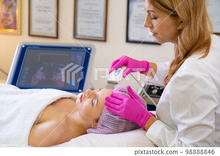 Woman in a spa salon on cosmetic procedures for facial care. Beautician makes medical procedures using a professional equipment. Cosmetologist making a woman a therapeutic procedure on a face. . Woman in a spa salon on cosmetic procedures for facial care. Beautician makes medical procedures using a professional equipment. Cosmetologist making a woman a therapeutic procedure on a face. . 98888846