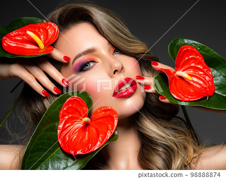 Beautiful white girl with red flowers. Stunning girl with Anthurium red. Closeup face of young beautiful blonde woman with a healthy clean skin. Pretty woman with bright makeup and long wavy hair. Beautiful white girl with red flowers. Stunning girl with Anthurium red. Closeup face of young beautiful blonde woman with a healthy clean skin. Pretty woman with bright makeup and long wavy hair. 98888874