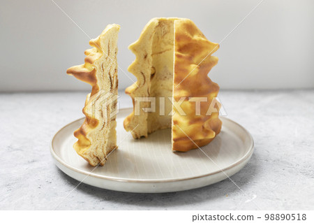 Cut piece of Sakotis ,sekacz, baumkuchen, traditional spit cake in lithuanian, polish, german, belarusian cuisine made of butter,eggs,flour,sugar, cooked on spit over open fire. Horizontal plane Cut piece of Sakotis ,sekacz, baumkuchen, traditional spit cake in lithuanian, polish, german, belarusian cuisine made of butter,eggs,flour,sugar, cooked on spit over open fire. Horizontal plane 98890518