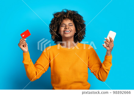 Emotional young african woman holding cell phone and credit card 98892666
