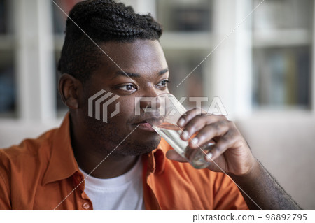 Closeup of happy black guy drinking water at home 98892795