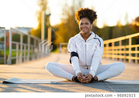 Sporty african american female stretching outdoors on yoga mat Sporty african american female stretching outdoors on yoga mat 98892815