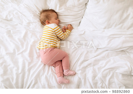 Top view of adorable baby girl sleeping on side in bed on white bedding, free copy space 98892860