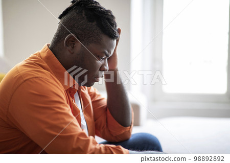 Side view of upset african american guy sitting at home Side view of upset african american guy sitting at home 98892892