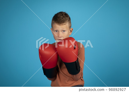 Portrait of motivated preteen boy wearing boxing gloves posing over blue background 98892927