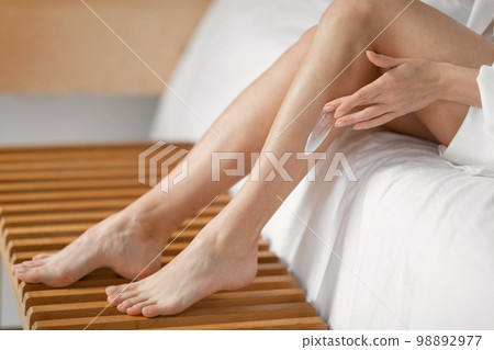 Millennial european woman applies cream on her legs, enjoys daily procedures in bedroom interior alone 98892977