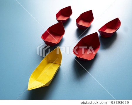 Leadership Concept - Yellow color paper ship origami leading the rest of the red paper ship on blue cover background. Copy space 98893629