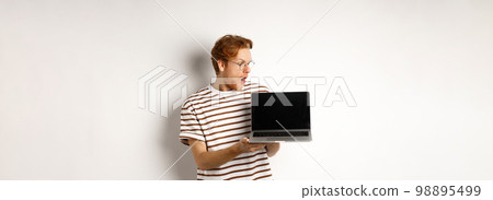 Young redhead man look impressed, showing laptop empty screen with logo banner. Guy in glasses checking out online advertisement on computer, white background 98895499