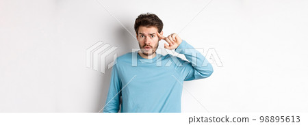 Annoyed caucasian man roll finger on temple, are you stupid or crazy gesture, scolding someone acting strange, standing in sweatshirt over white background 98895613