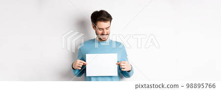 Young caucasian man looking at empty paper, reading logo, standing on white background Young caucasian man looking at empty paper, reading logo, standing on white background 98895766
