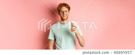 Happy redhead man in glasses and t-shirt drinking coffee and smiling, enjoying lunch break, holding takeaway cup, standing over pink background Happy redhead man in glasses and t-shirt drinking coffee and smiling, enjoying lunch break, holding takeaway cup, standing over pink background 98895957